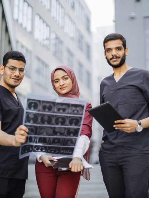 Three doctors, woman in hijab and two men in medical apparel, discussing patient's x-ray CT scan