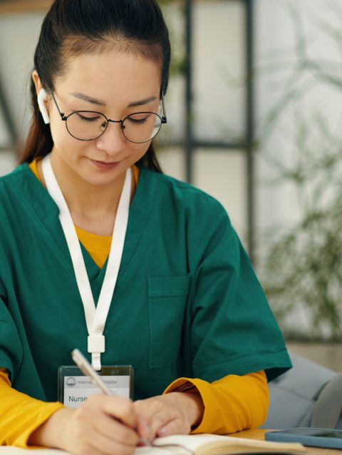 Writing Notes in Green Scrubs Sitting at Desk