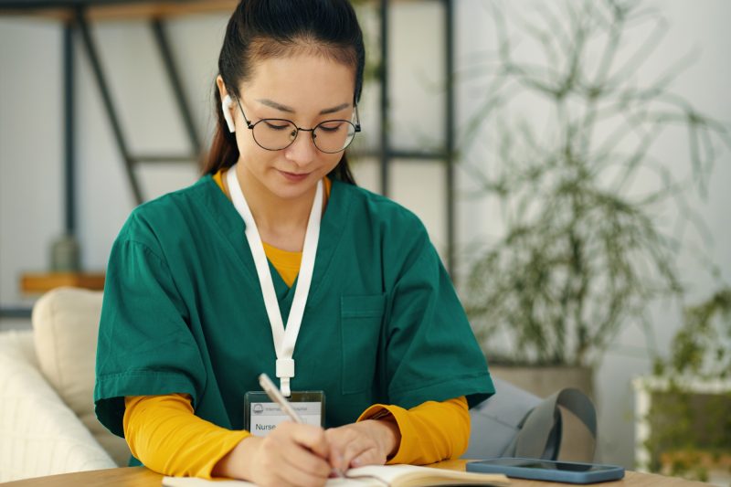 Writing Notes in Green Scrubs Sitting at Desk