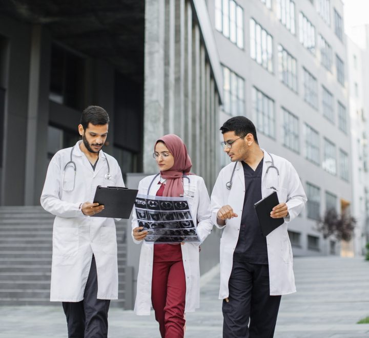 Three doctors, woman in hijab and two men in medical apparel, discussing patient's x-ray CT scan